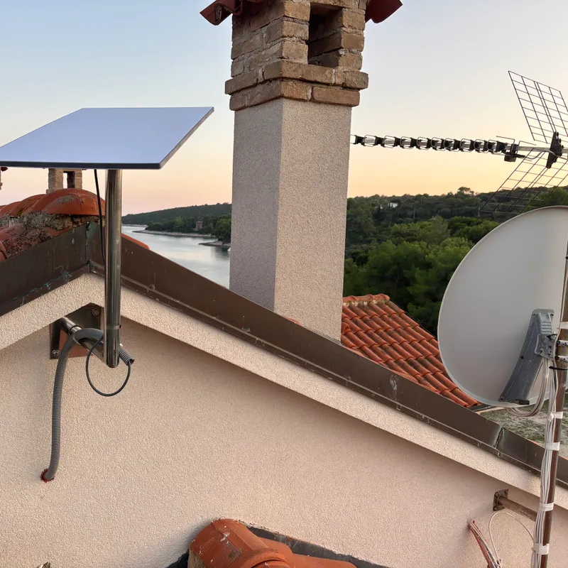 Starlink antena montirana uz dimnjak na kosom krovu